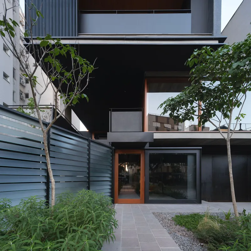 Ground level courtyard with paved tiles, young trees and timber-framed glass doors set in black walls