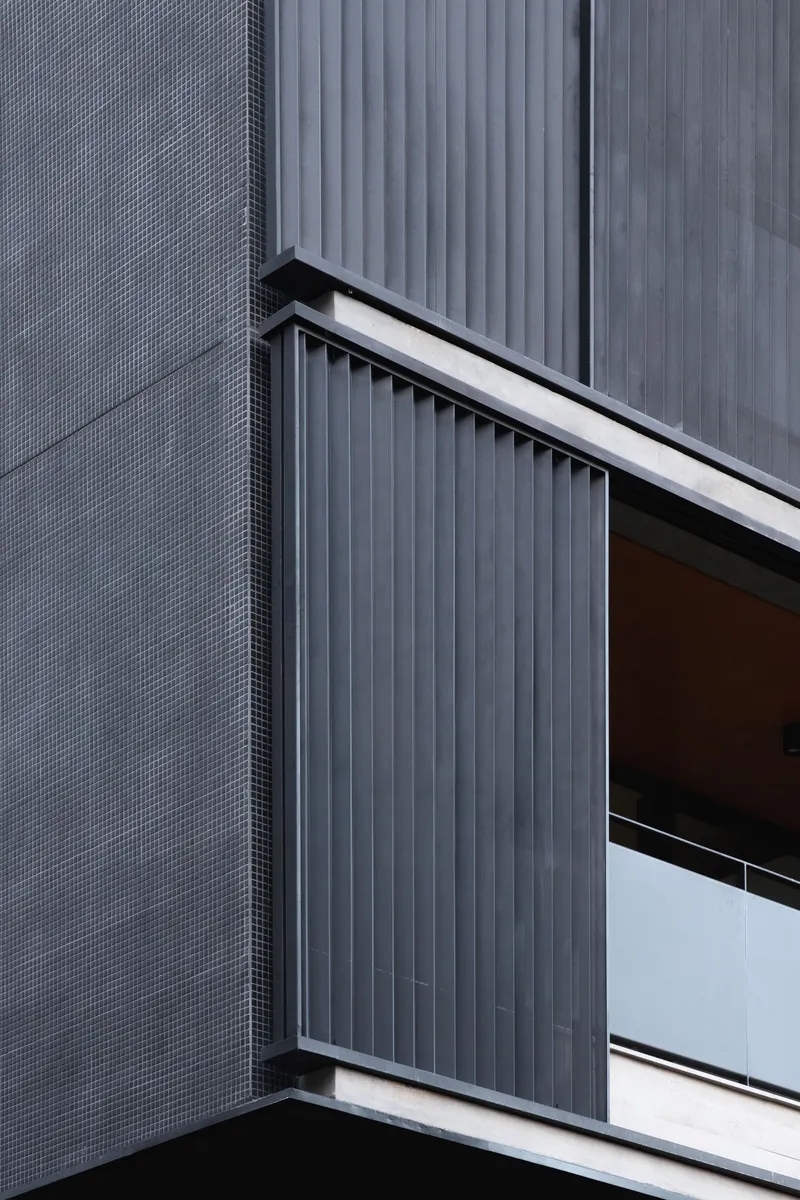 Balcony detail showing vertical corrugated metal screen beside textured grey tile cladding and white guardrail edge