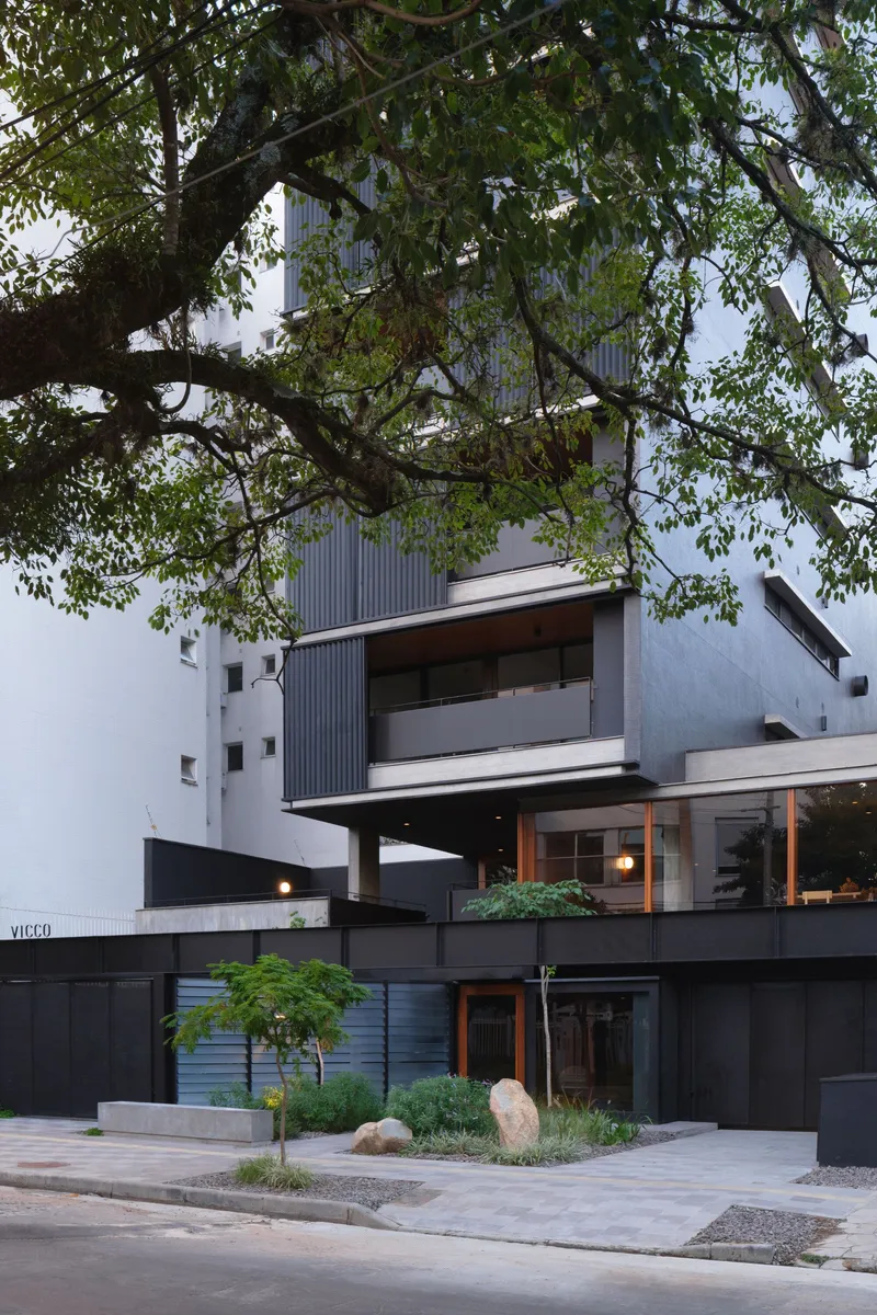 Street view of the stacked volumes with corrugated metal cladding framed by overhanging tree branches at dusk