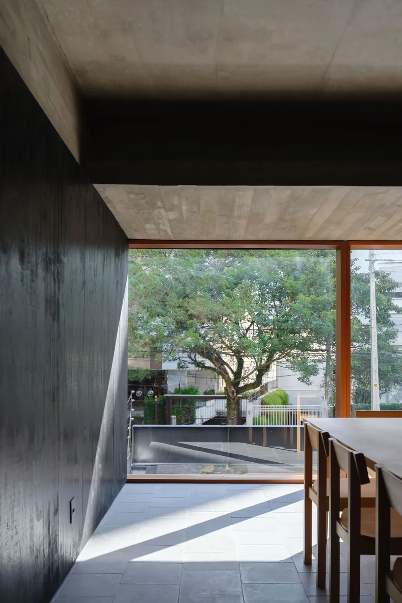 Dining area with exposed concrete ceiling and beams framing views of the tree canopy through timber windows