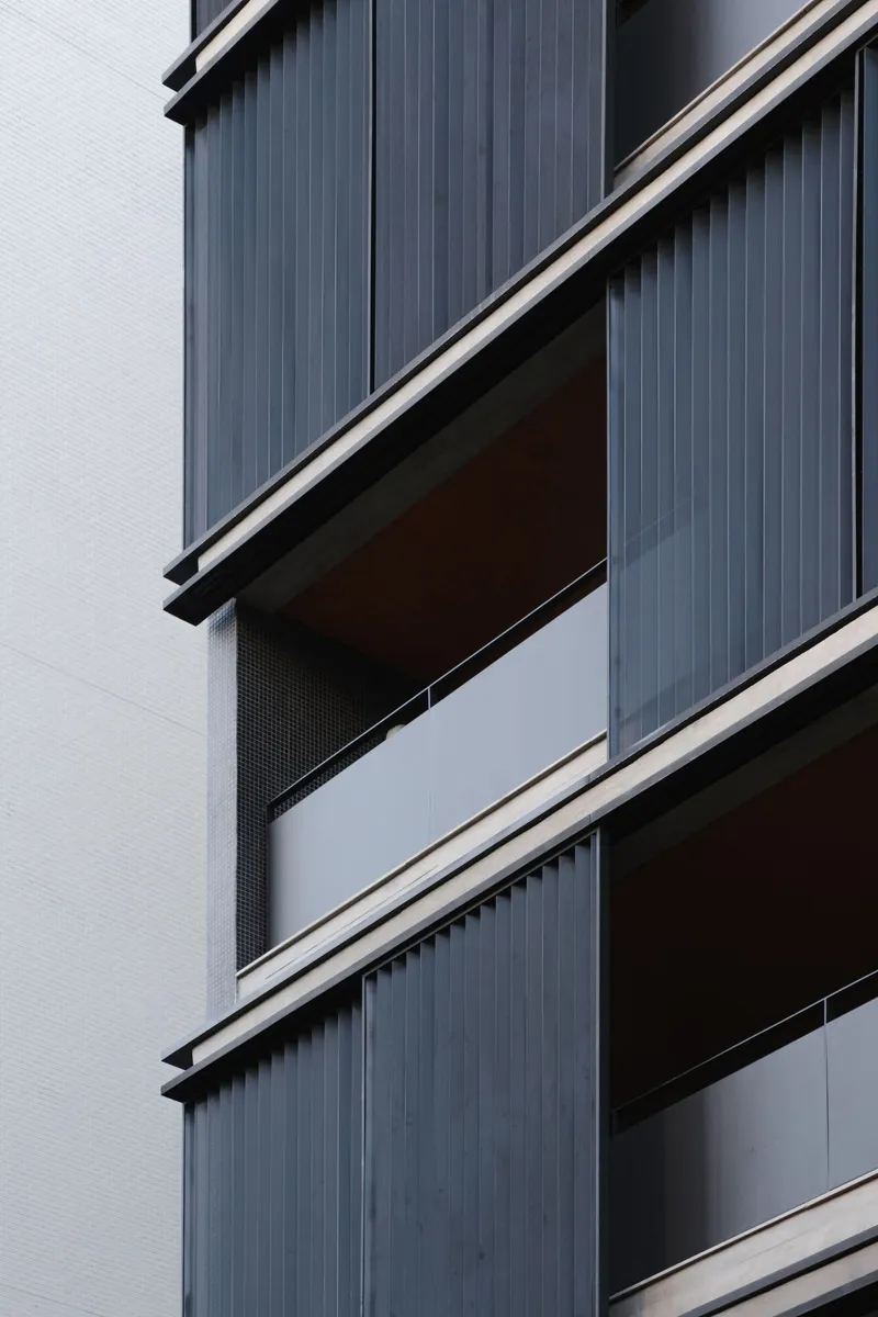 Detail of the stacked balconies with vertical corrugated metal panels and perforated metal screens on overcast day