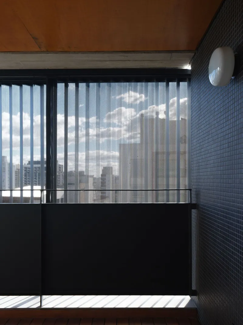 Balcony corner with blue mosaic tile wall, timber soffit, and sheer curtains filtering bright daylight