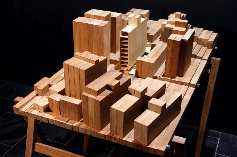Wooden massing model showing clustered towers and mid-rise volumes on a black background