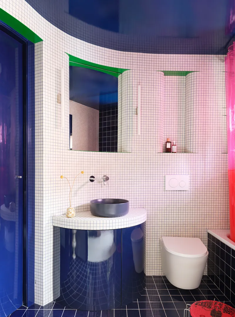 Bathroom with white mosaic tile walls, curved mirrors with green frames, and blue reflective surfaces
