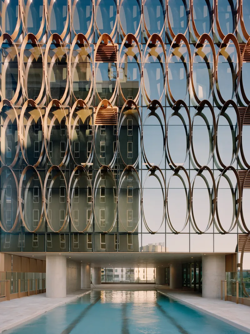 Ground-level pool terrace framed by the bronze oval-patterned screen facade above white columns
