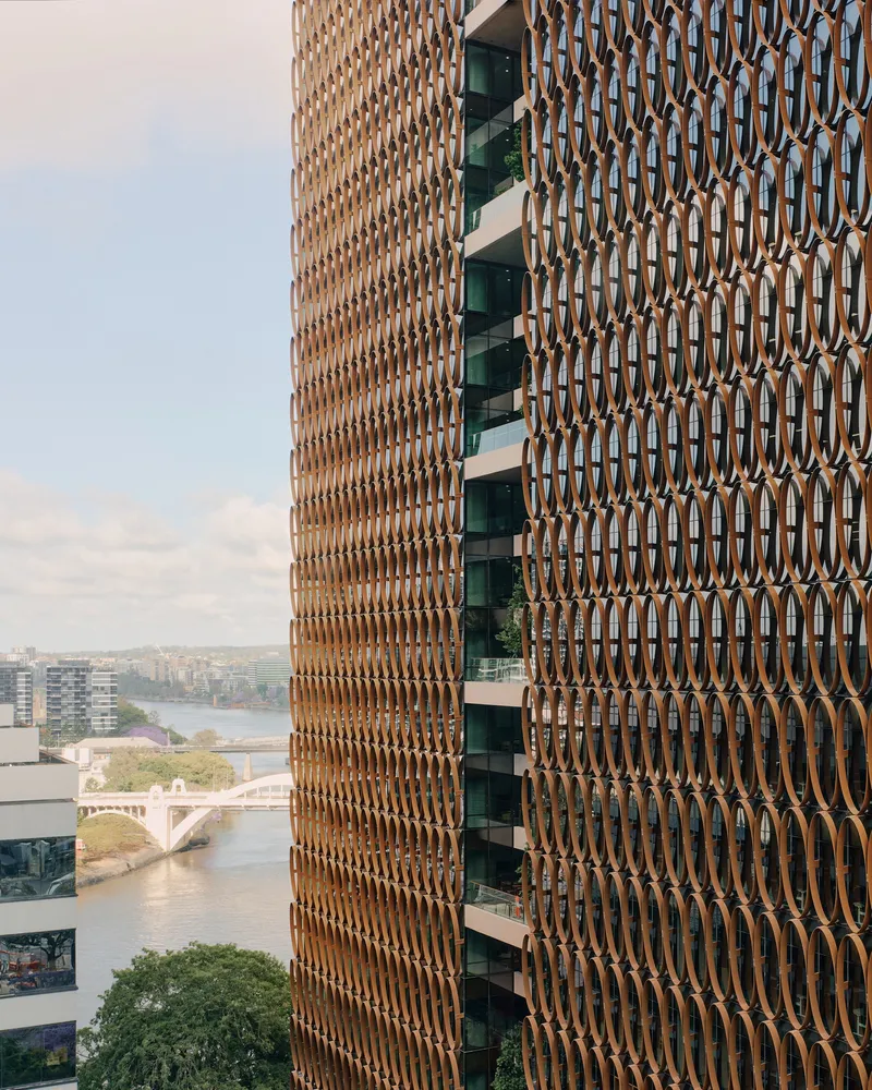Curved tower facade with repeating bronze oval screens and recessed balconies overlooking the river below
