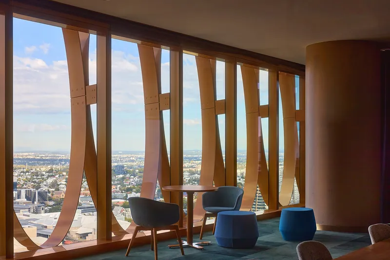 Interior lounge with curved timber screen and blue upholstered chairs overlooking the cityscape through floor-to-ceiling windows