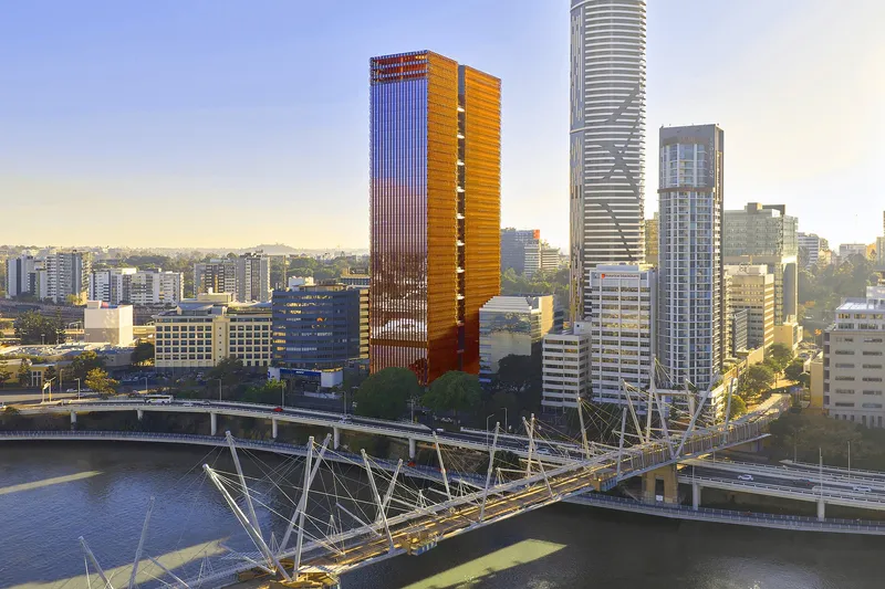 Aerial view of two high-rise towers with vertical bronze louvres beside a pedestrian bridge at dusk