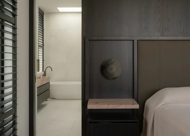 Bedroom with timber-framed sleeping niche and adjacent ensuite bathroom glimpsed through doorway with horizontal louvres
