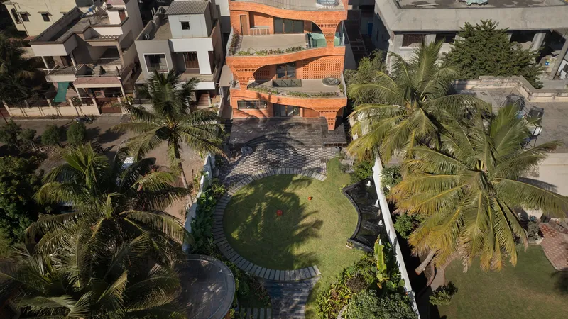 Aerial view of the curved terracotta residence with tiered garden and surrounding palm trees