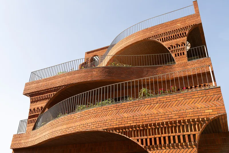 Close-up of the layered brick facade showing chevron patterns and curved balconies with metal railings