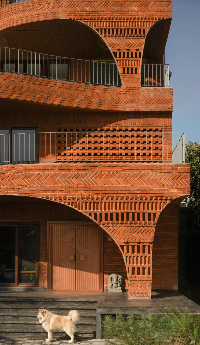 Layered terracotta brick patterns with perforated screens and timber door at ground level with dog