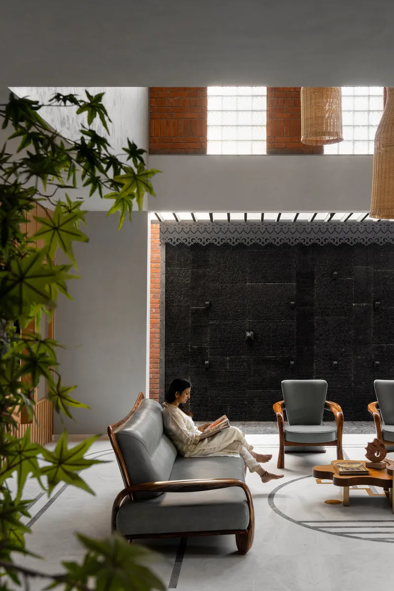 Interior courtyard with woman reading on lounge chair beneath clerestory windows and black tile wall