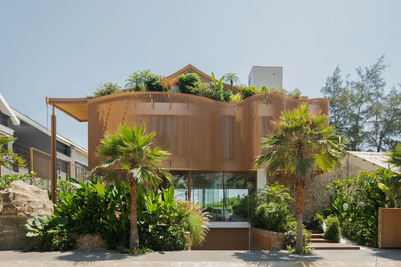 Vertical timber screen facade with rooftop planting and palms framing the entry below