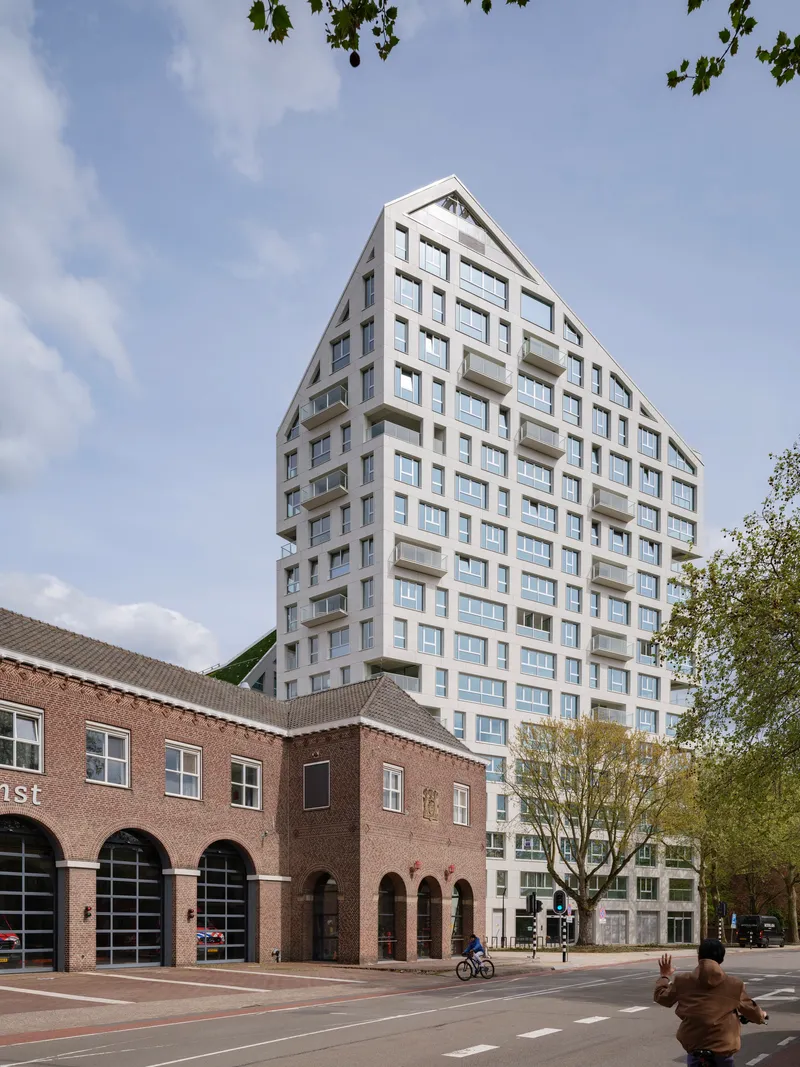 Street view of the white tower with recessed balconies rising above a historic brick arcade and a cyclist