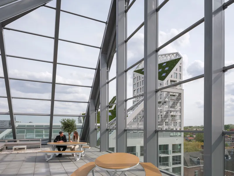Glazed interior terrace with angled structural mullions framing views of the planted roofs and neighboring towers