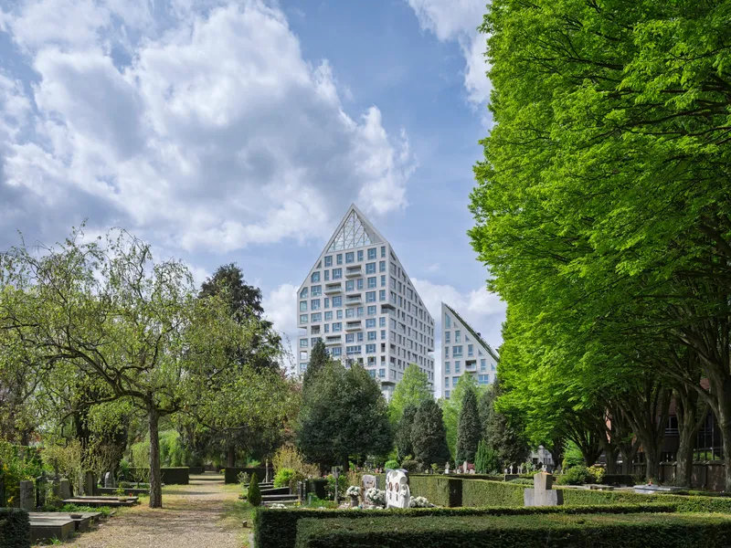 Twin gabled towers rising above a park cemetery with trimmed hedges and spring foliage