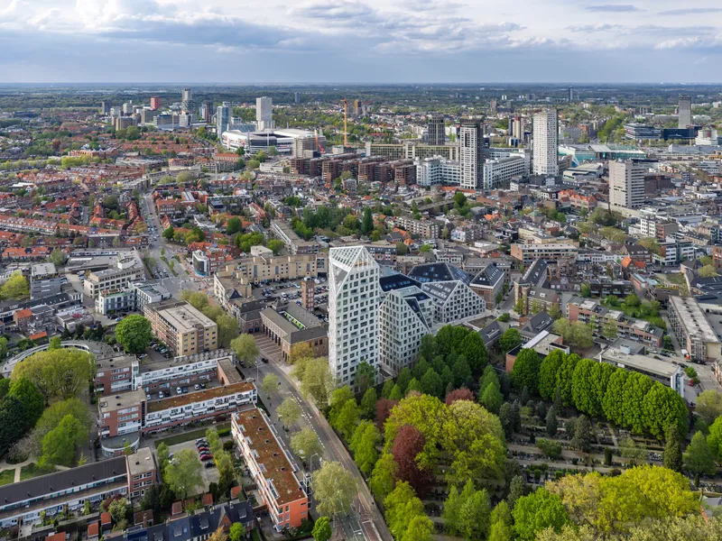 Distant aerial perspective of white faceted towers positioned among treetops and low-rise residential blocks