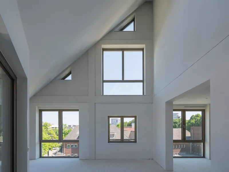 Double-height interior with pitched ceiling, clerestory windows, and varied apertures framing neighboring rooftops