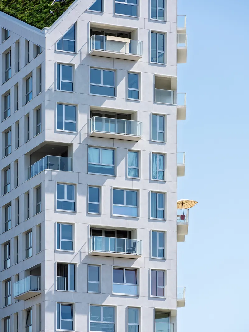 White facade with staggered balconies and glazed openings showing yellow umbrella on upper terrace