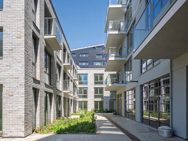 Courtyard passageway between brick facades with projecting balconies and planted beds in bright sunlight
