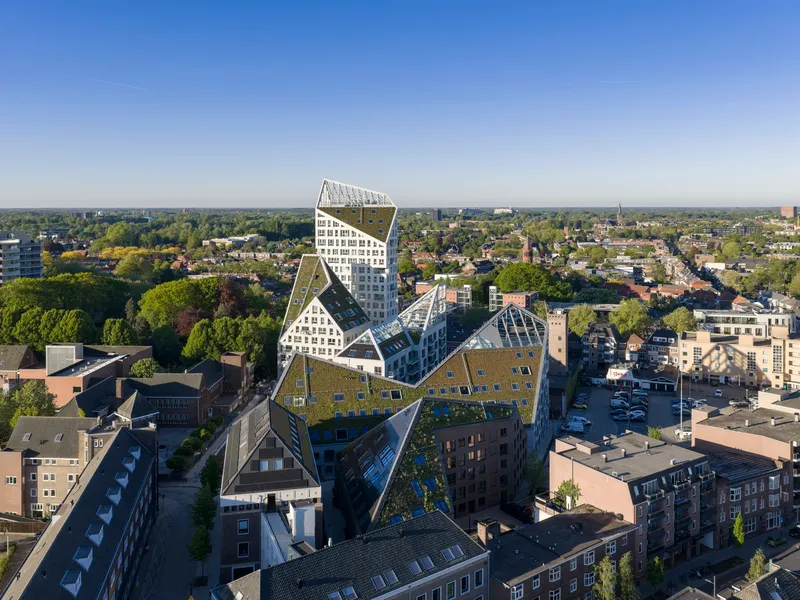 Aerial view of the zigzag pitched roof volumes with green roofs rising above low-rise urban blocks