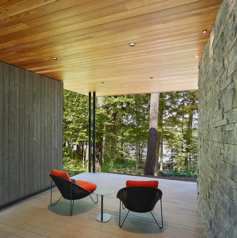 Covered terrace with timber decking and stacked stone wall overlooking forested landscape