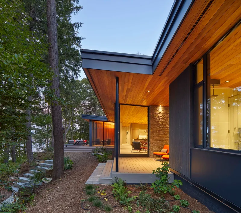 Exterior view of timber-clad overhang and glass walls nestled among conifer trees at dusk