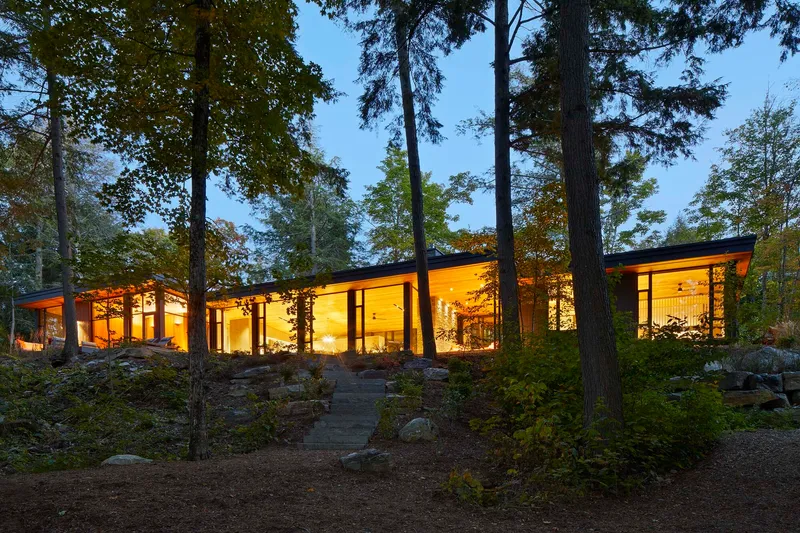 Long glass facade glowing at dusk with steel columns framing views into interior spaces