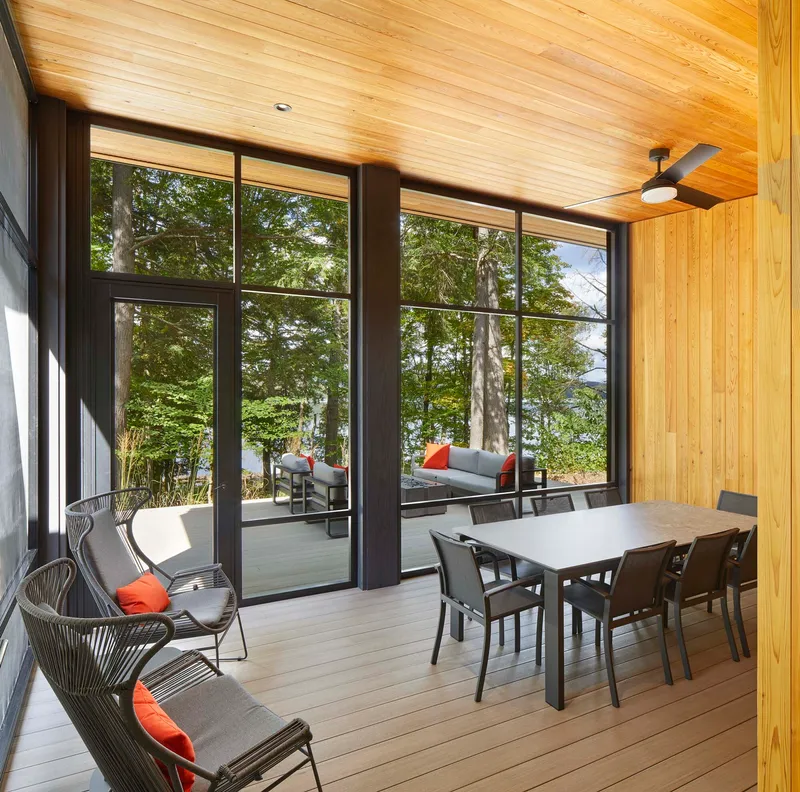Screened porch with composite decking, timber ceiling, and steel-framed glazing overlooking the forest