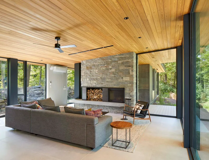 Living room with stacked stone fireplace, wood nook, and large glazed openings on two sides