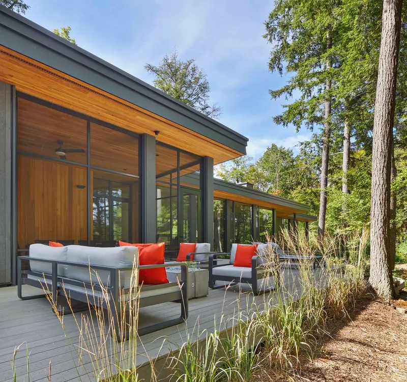 Outdoor terrace with seating adjacent to floor-to-ceiling glazing and timber soffits under a clear sky