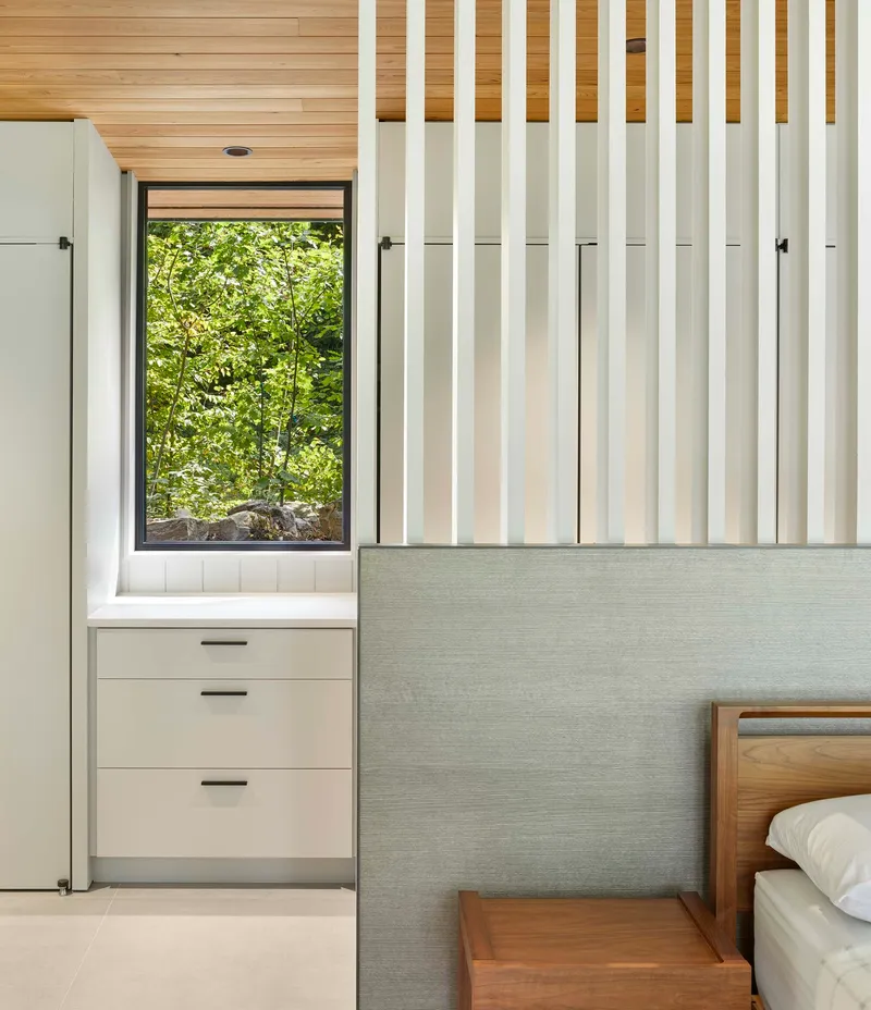 Built-in storage wall with vertical slat detail and window framing green foliage outside