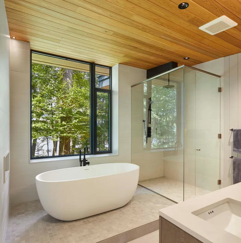 Bathroom with freestanding tub beneath timber slat ceiling and floor-to-ceiling window overlooking trees