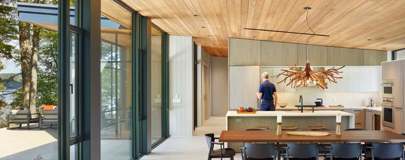 View from dining area through sliding glass doors to outdoor terrace with person moving through kitchen