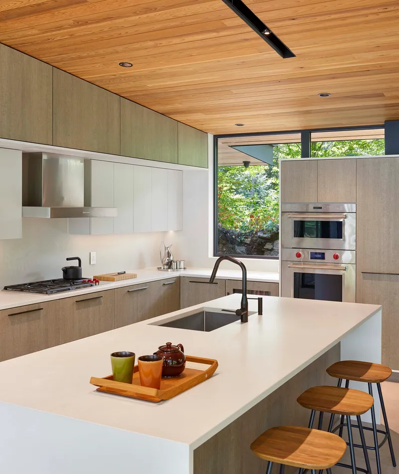 Kitchen island with white countertop and timber cabinetry beneath wood plank ceiling with skylight slot