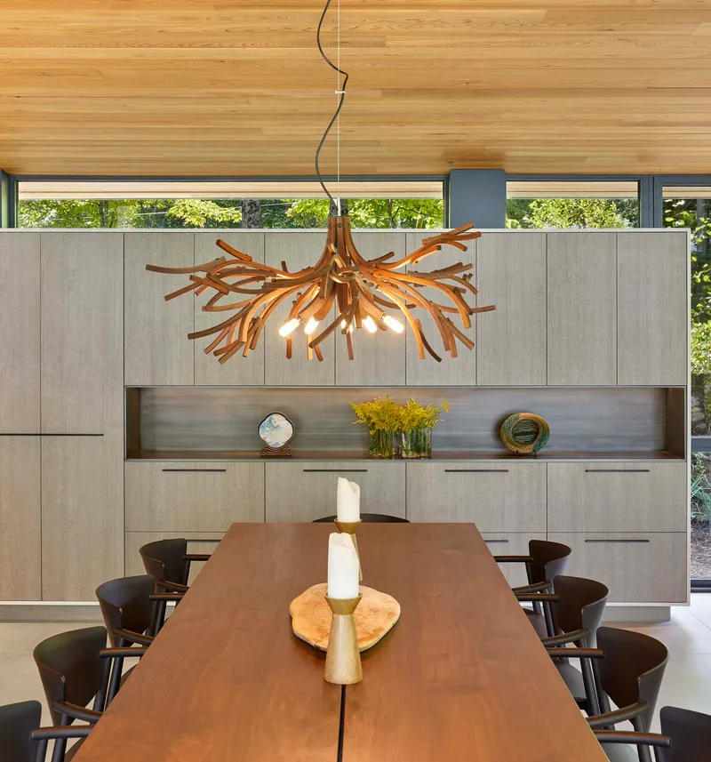 Dining room with sculptural branch chandelier above walnut table and pale grey paneled cabinetry