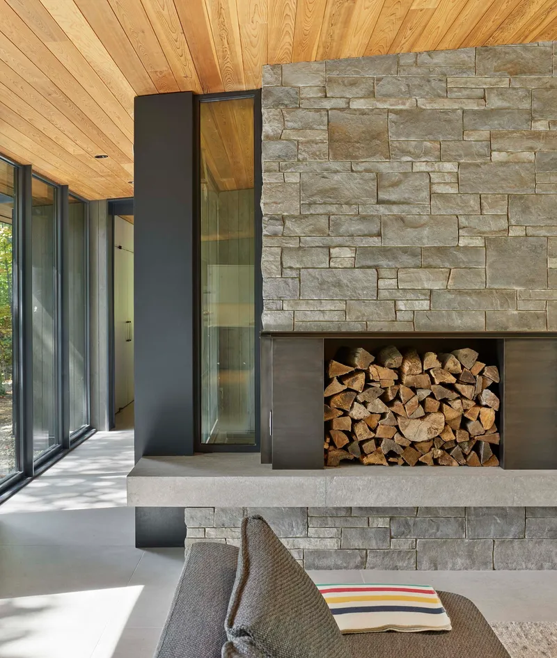 Stacked limestone fireplace with steel-framed firewood niche beneath timber plank ceiling