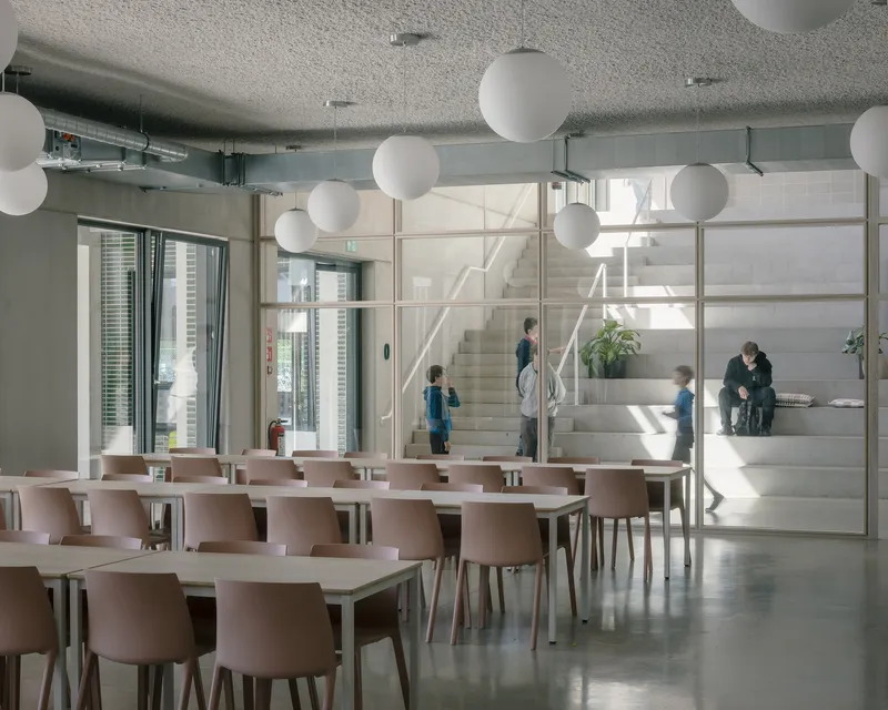 Dining area with pink chairs and globe pendant lights overlooking a glazed stairwell with children moving through