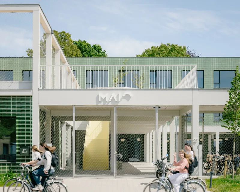 Main entrance with white metal pergola and mesh screens as cyclists pass by