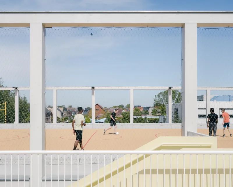 Rooftop sports court framed by white steel columns and mesh netting with players in afternoon light