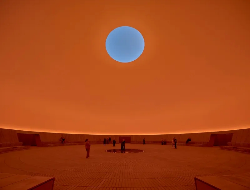 The same circular courtyard space illuminated with warm orange light and visitors on the floor