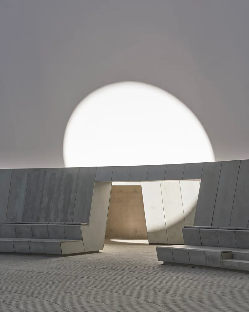 Courtyard portal framing a distant stone volume beneath a monumental circular oculus in the sky