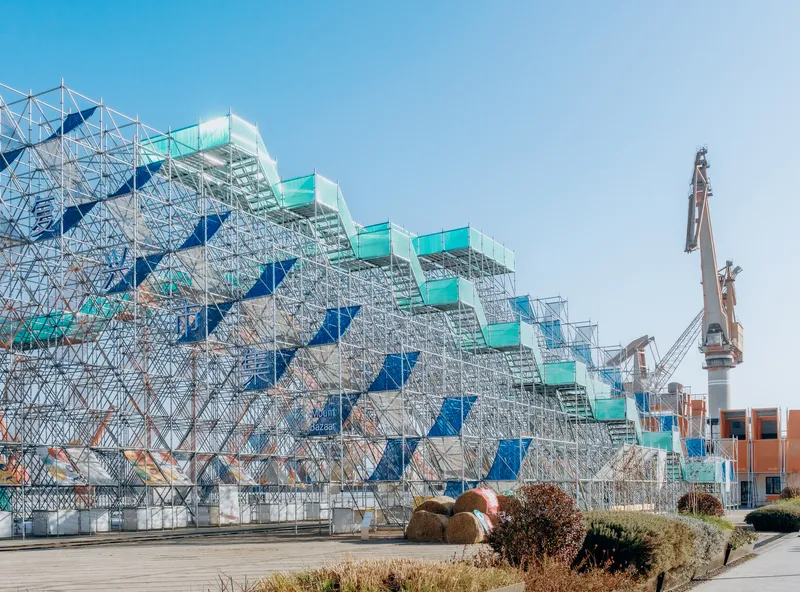 Side elevation of the steel scaffolding with blue infill panels and turquoise platform treads above