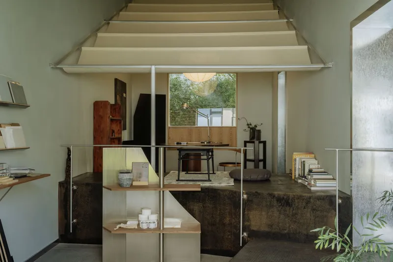 Double-height interior with exposed timber beam ceiling and a central platform beneath a framed courtyard view