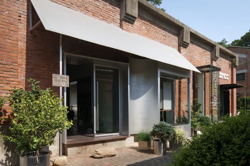 White-framed entrance set within an existing brick facade with potted plants on a paved courtyard