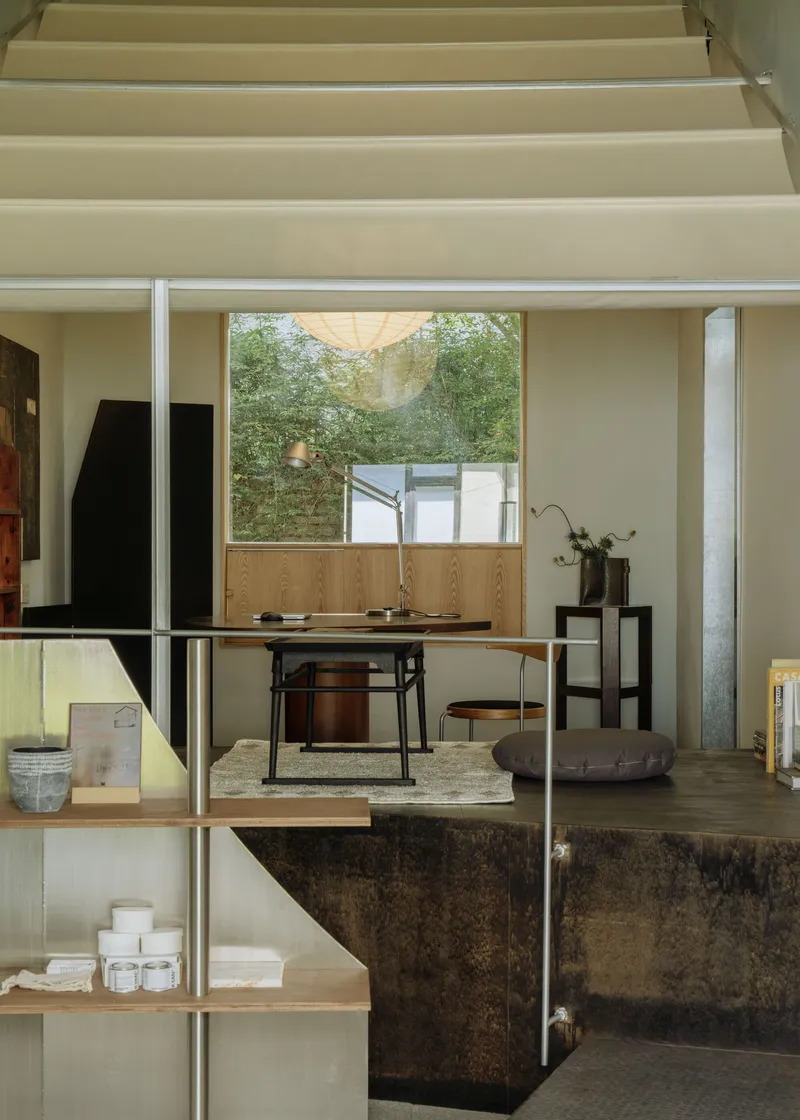View across glass and timber shelving toward a raised platform with dining table below a courtyard window