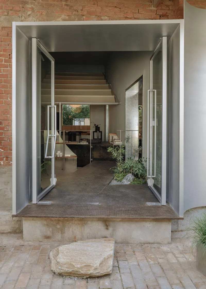 Open steel-framed pivot doors revealing an interior with raised platform and exposed brick walls beyond