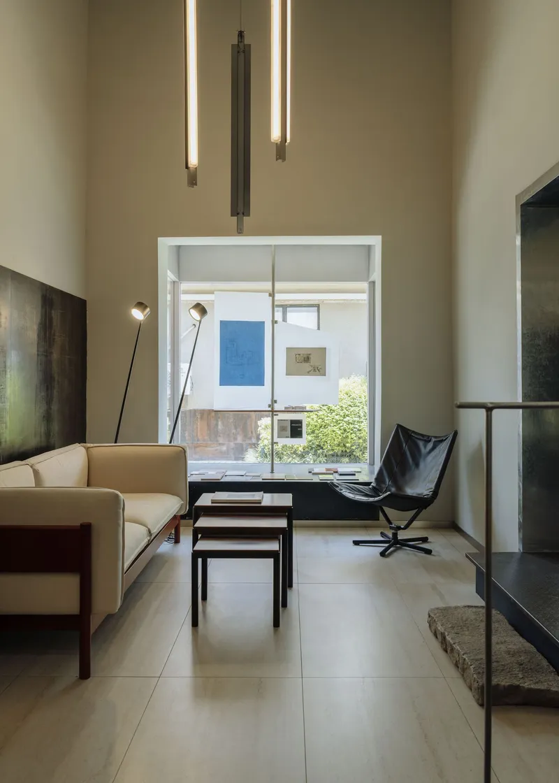 Living room with tall ceiling and tubular pendant lights overlooking a planted courtyard through glazed opening