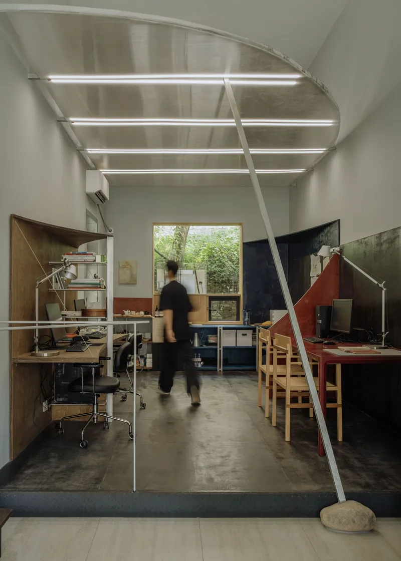 Studio workspace with vaulted steel ceiling and a person walking past workstations under linear lighting